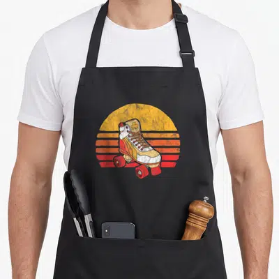 Tablier de cuisine noir avec une patinette vintage devant un soleil rayé orange et rouge.