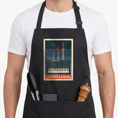 Tablier de cuisine noir avec illustration synthétisateur soviétique, fusées rouges et texte cyrillique en rouge.