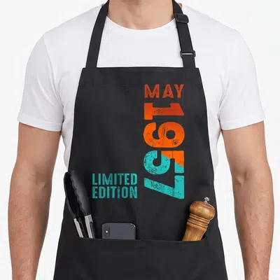 Tablier de cuisine noir avec typographie verticale orange et turquoise indiquant Mai 1957 et Limited Edition.