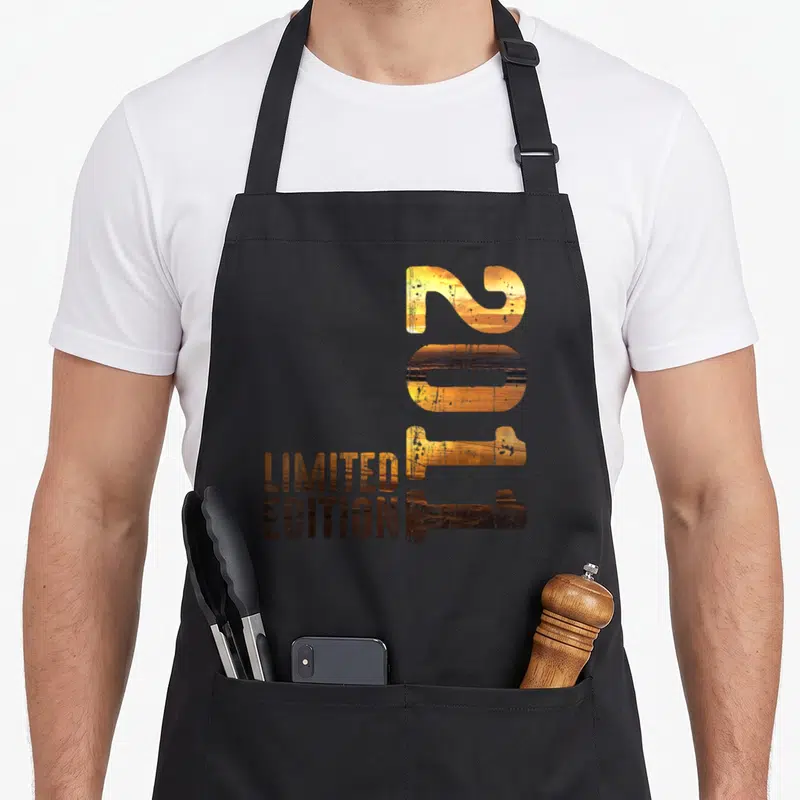 Tablier de cuisine noir avec le chiffre 2011 en lettres orange sunset et Limited Edition en brun.