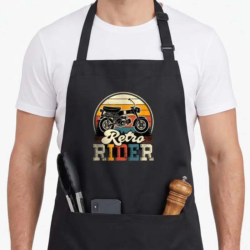 Tablier de cuisine noir avec illustration cyclomoteur rétro et texte Retro Rider coloré sur fond arc-en-ciel.