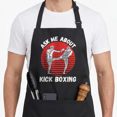 Tablier de cuisine noir avec illustration rétro de kick boxeurs et texte Ask Me About Kick Boxing en blanc sur fond rouge.