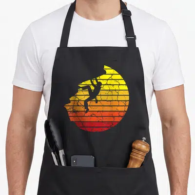 Tablier de cuisine noir avec silhouette d'escaladeur sur fond de soleil dégradé jaune orange rouge effet rétro