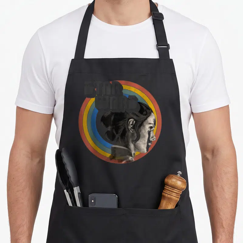 Tablier de cuisine noir avec illustration rétro de Rey et logo Star Wars dans un cercle coloré.