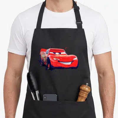 Tablier de cuisine noir avec une illustration de Lightning McQueen aux couleurs vives et des éclaboussures artistiques bleues autour du véhicule.