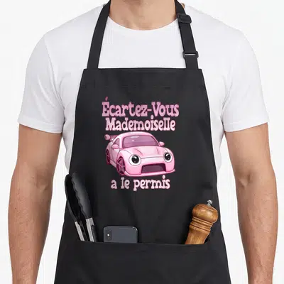 Tablier de cuisine noir avec une voiture rose dessinée et le texte Écartez-Vous Mademoiselle a le permis en lettres roses.