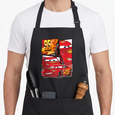 Tablier de cuisine noir avec Lightning McQueen 95, flammes orange et visages expressifs en collage graphique.