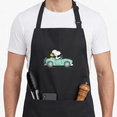 Tablier de cuisine noir avec Snoopy conduisant une voiture verte avec Woodstock à côté.