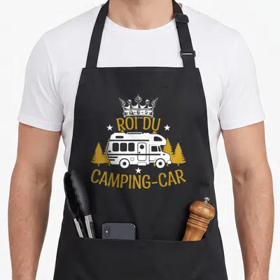 Tablier de cuisine noir avec illustration d'un camping-car blanc sous une couronne et le texte Roi du camping-car en lettres dorées.