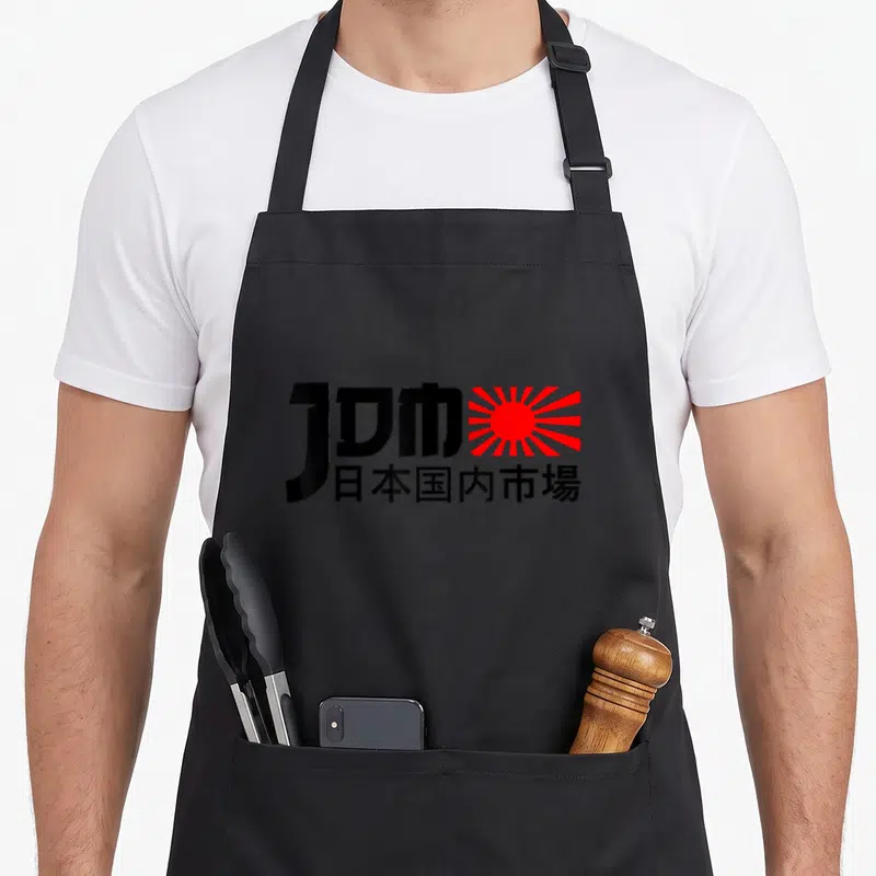 Tablier de cuisine noir avec logo JDM et soleil levant rouge sur fond uni.