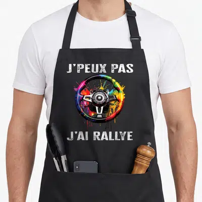 Tablier de cuisine noir avec un volant multicolore et le texte J'peux pas j'ai rallye imprimé en blanc.