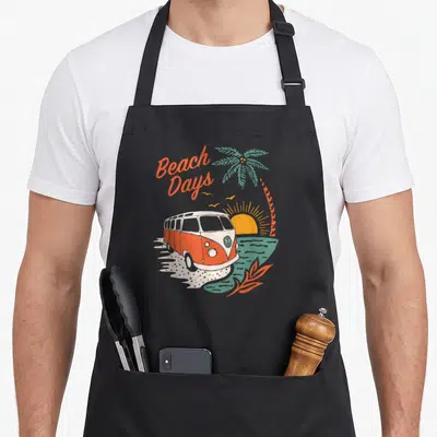 Tablier de cuisine noir avec illustration camping-car T1 orange, palmier et texte Beach Days en orange.