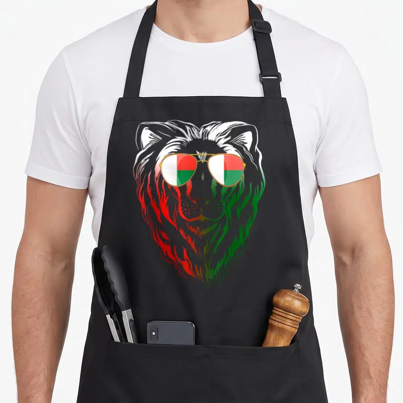 Tablier de cuisine noir avec tête de lion aux verres de lunettes affichant les couleurs du drapeau malgache.