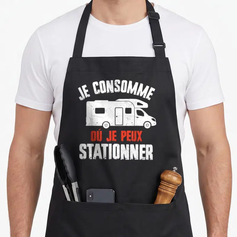 Tablier de cuisine noir avec illustration de camping-car et texte Je consomme où je peux stationner en blanc et rouge.