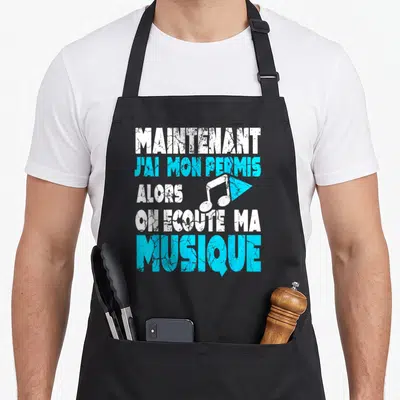 Tablier de cuisine noir avec inscription blanche et bleue maintenant j'ai mon permis alors on écoute ma musique et une note musicale.