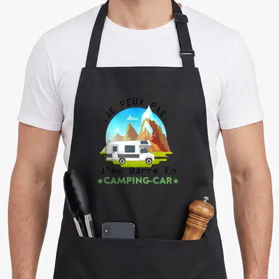 Tablier de cuisine noir avec illustration d'un camping-car blanc devant des montagnes et le texte Je peux pas Jme Barre En Camping-car.
