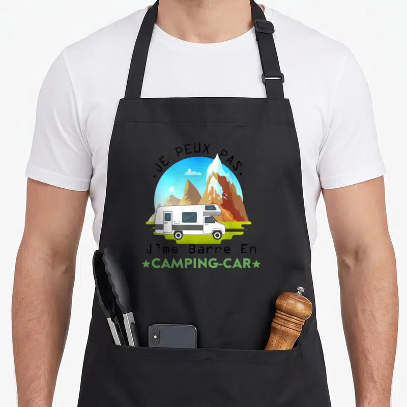 Tablier de cuisine noir avec illustration d'un camping-car blanc devant des montagnes et le texte Je peux pas Jme Barre En Camping-car.