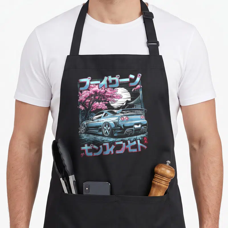 Tablier de cuisine noir avec illustration d'une voiture japonaise bleue, de fleurs de sakura roses et de texte en caractères japonais.