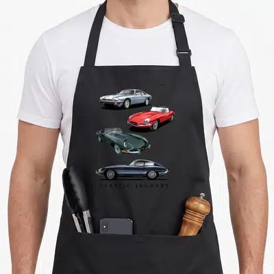 Tablier de cuisine noir avec quatre illustrations de voitures de sport britanniques et l'inscription Classic Jaguars en bas.