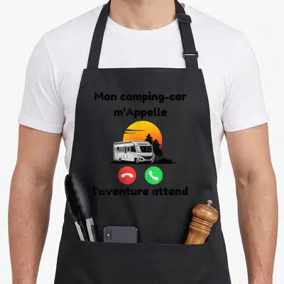 Tablier de cuisine noir avec illustration d'un camping-car, un soleil orange et les mots Mon camping-car m'Appelle l'aventure attend.