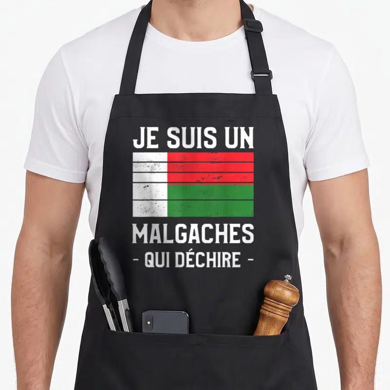 Tablier de cuisine noir avec texte blanc et drapeau malgache stylisé effet délavé au centre.