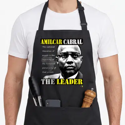 Tablier de cuisine noir avec portrait d'Amilcar Cabral, texte The Leader et carte de l'Afrique en arrière-plan discret.