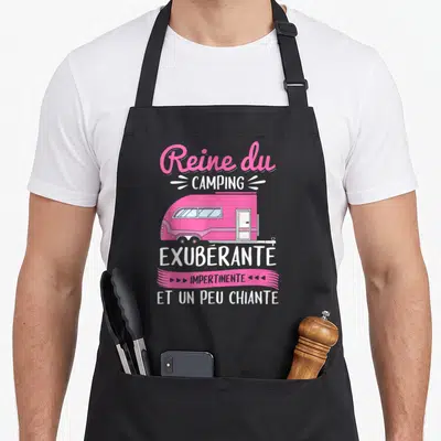 Tablier de cuisine noir avec illustration caravane rose et texte Reine du camping exubérante impertinente.