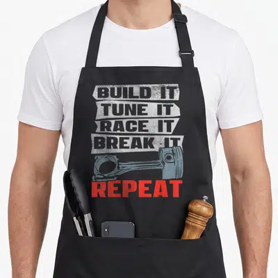 Tablier de cuisine noir avec le texte Build It Tune It Race It Break It Repeat et un piston bleu en arrière-plan.