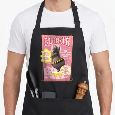 Tablier de cuisine noir avec une illustration circique rose représentant Gloria hippopotame en tenue dorée.