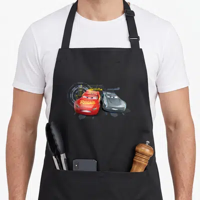 Tablier de cuisine noir avec Lightning McQueen rouge et Jackson Storm gris en course.