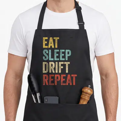 Tablier de cuisine noir avec l'inscription Eat Sleep Drift Repeat en lettres colorées style vintage.
