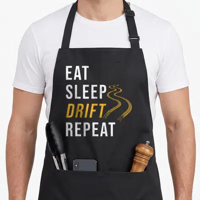 Tablier de cuisine noir avec texte Eat Sleep Drift Repeat et traces de pneu jaunes sinueuses sur le côté droit.