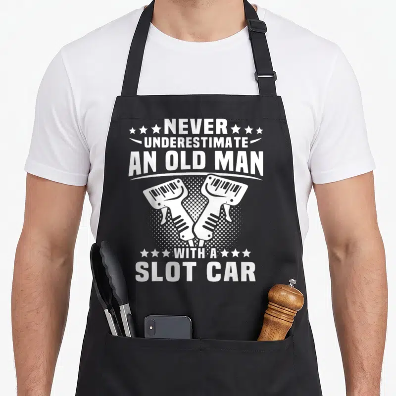 Tablier de cuisine noir avec texte blanc et illustration de deux manettes de slot car croisées.