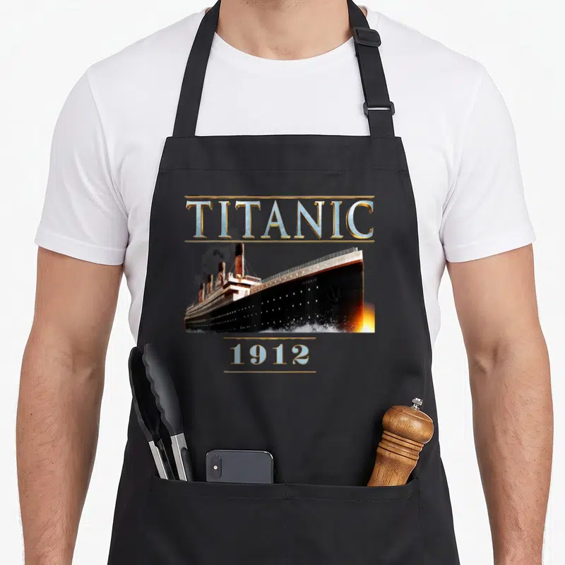 Tablier de cuisine noir avec illustration du paquebot Titanic 1912 et lettrage métallique doré.