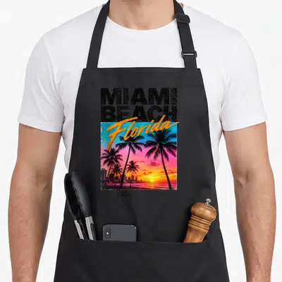 Tablier de cuisine noir avec illustration vintage Miami Beach Florida palmiers et coucher de soleil coloré sur fond dégradé.