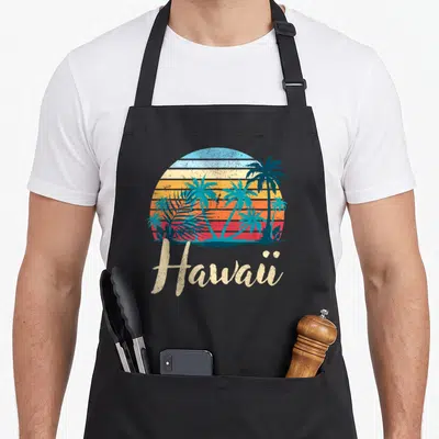 Tablier de cuisine noir avec illustration Hawaii palmiers et texte rétro coloré.