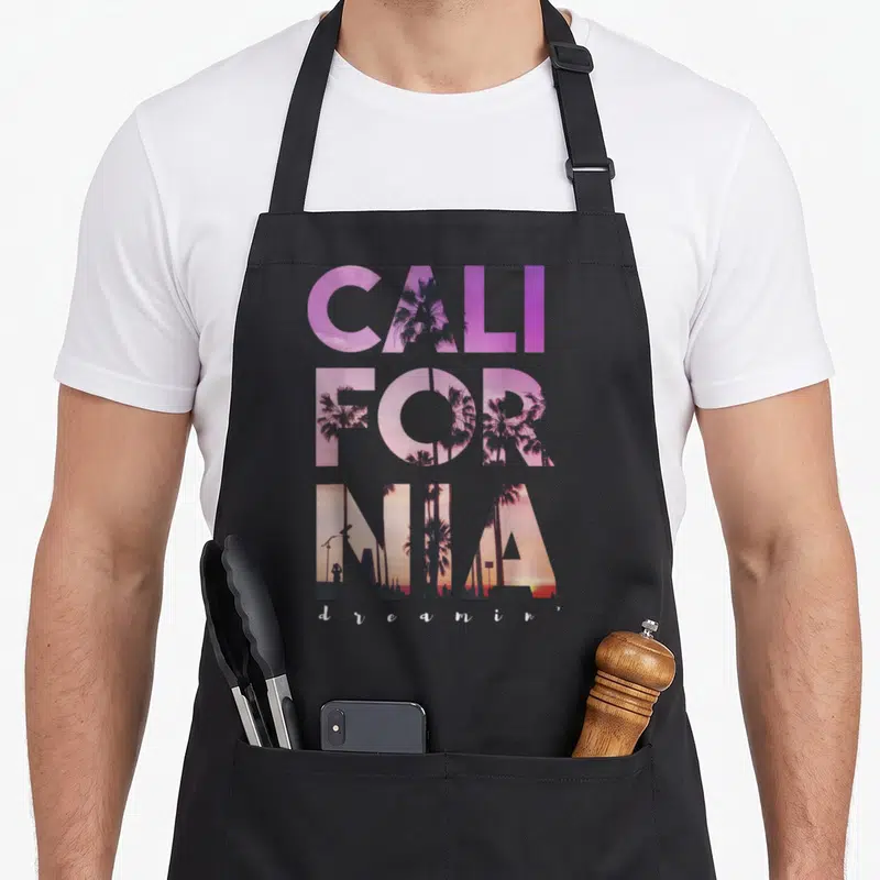 Tablier de cuisine noir avec typographie colorée CALIFORNIA et silhouettes de palmiers au coucher du soleil.