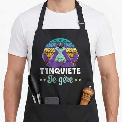 Tablier de cuisine noir avec un fourrureux violet en position lotus et le texte T'inquiète je gère sur fond coloré rétro.