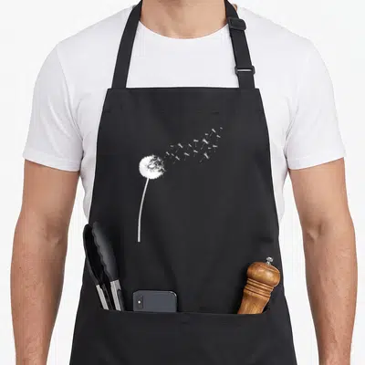 Tablier de cuisine noir avec illustration blanche d'un pissenlit dont les graines s'envolent vers la droite.