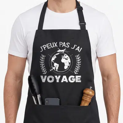 Tablier de cuisine noir avec inscription blanche J'peux pas j'ai voyage surmontant une illustration de globe terrestre et d'avions.
