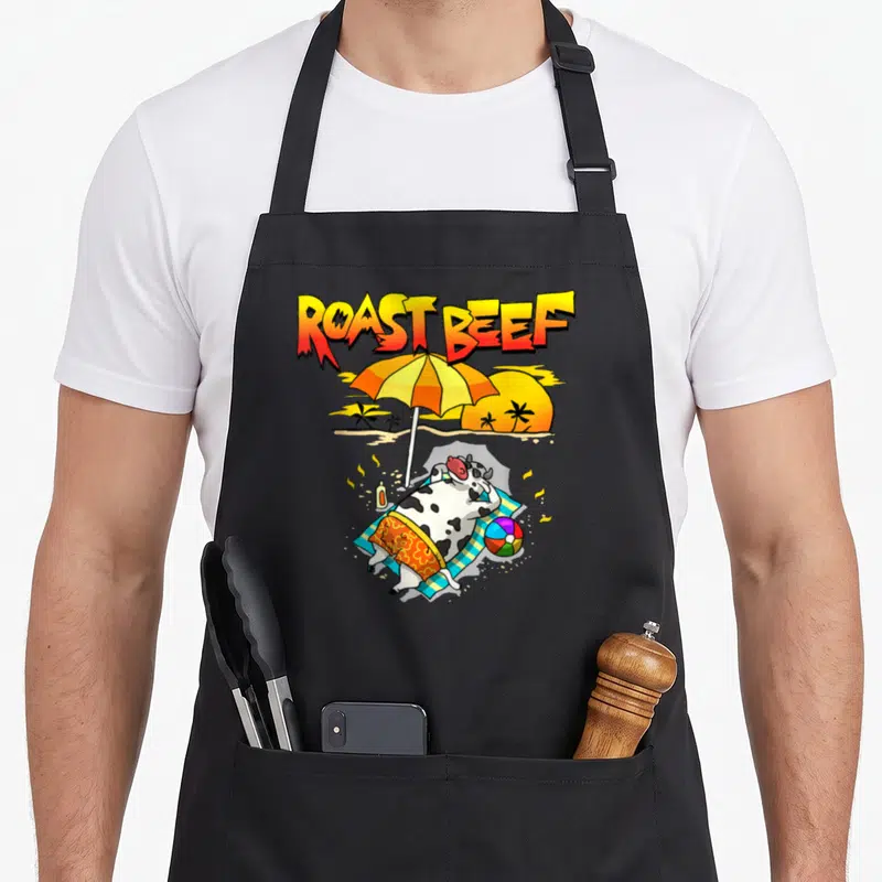 Tablier de cuisine noir avec une vache bronzant sous un parasol et le texte Roast Beef au-dessus.