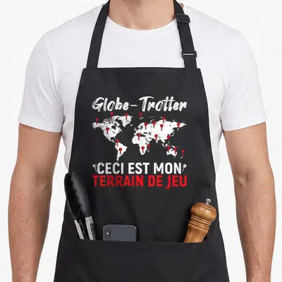 Tablier de cuisine noir avec carte du monde blanche, repères rouges et inscription ceci est mon terrain de jeu en blanc et rouge.