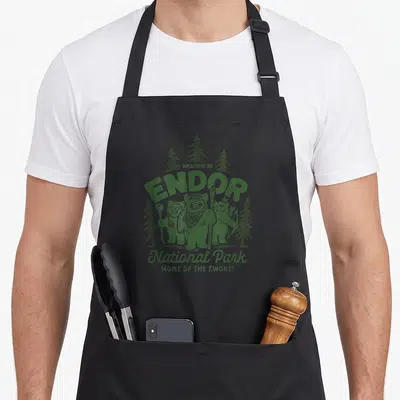 Tablier de cuisine noir avec illustration verte représentant trois Ewoks devant des sapins et le texte Welcome to Endor National Park Home of the Ewoks.