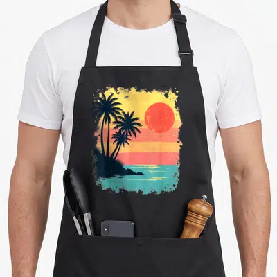 Tablier de cuisine noir avec illustration de palmiers et soleil couchant aux couleurs chaudes style rétro.