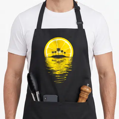Tablier de cuisine noir avec illustration d'un demi-citron jaune formant un soleil au-dessus d'une île aux palmiers et d'eau ondulée.