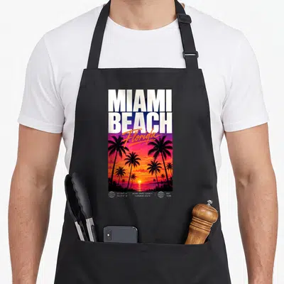Tablier de cuisine noir avec illustration de coucher de soleil Miami Beach Floride et silhouettes de palmiers tropicaux.