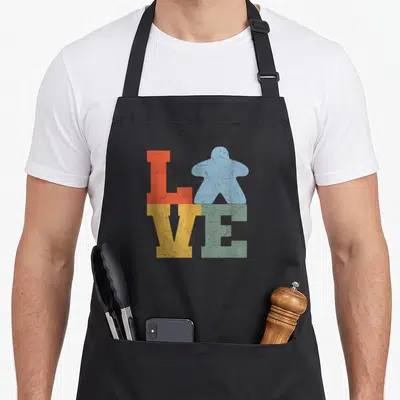 Tablier de cuisine noir avec le mot Love formé par des lettres colorées et une pièce de jeu bleue en forme de meeple.