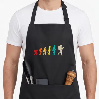 Tablier de cuisine noir avec silhouettes colorées représentant l'évolution humaine vers le voyageur avec sac à dos et carte.