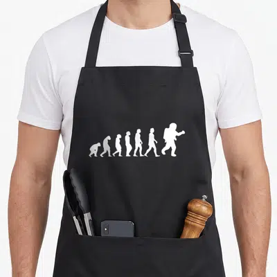 Tablier de cuisine noir avec une illustration blanche représentant l'évolution de l'homme se terminant par un astronaute.