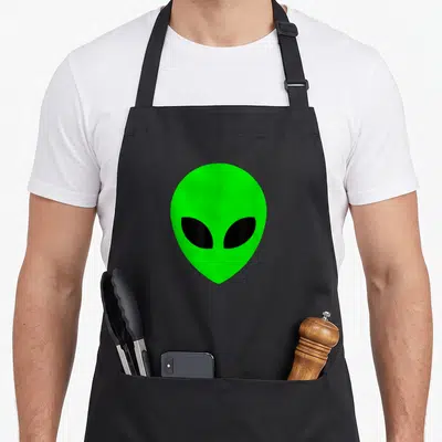 Tablier de cuisine noir avec une tête d'alien vert vif aux grands yeux noirs en forme d'amande